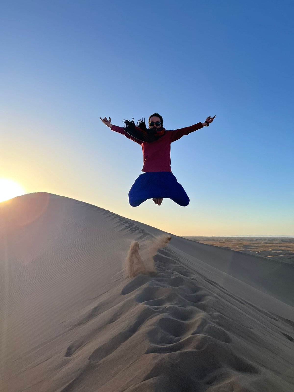 Amasir Voyage guide jumping on top of a sand dune at sunset